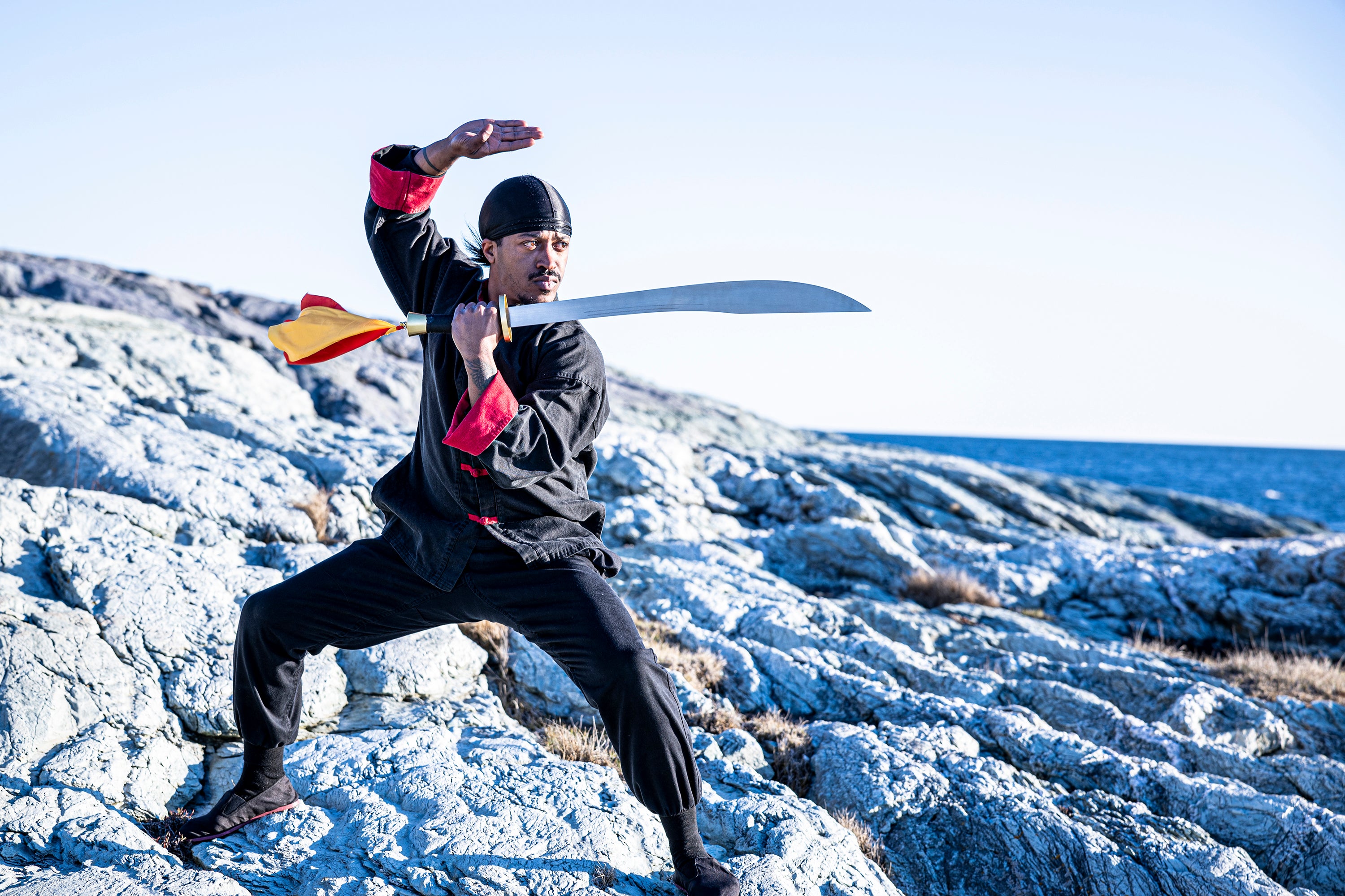 Rob Campbell with sword and in Kung Fu uniform on rocks near beach