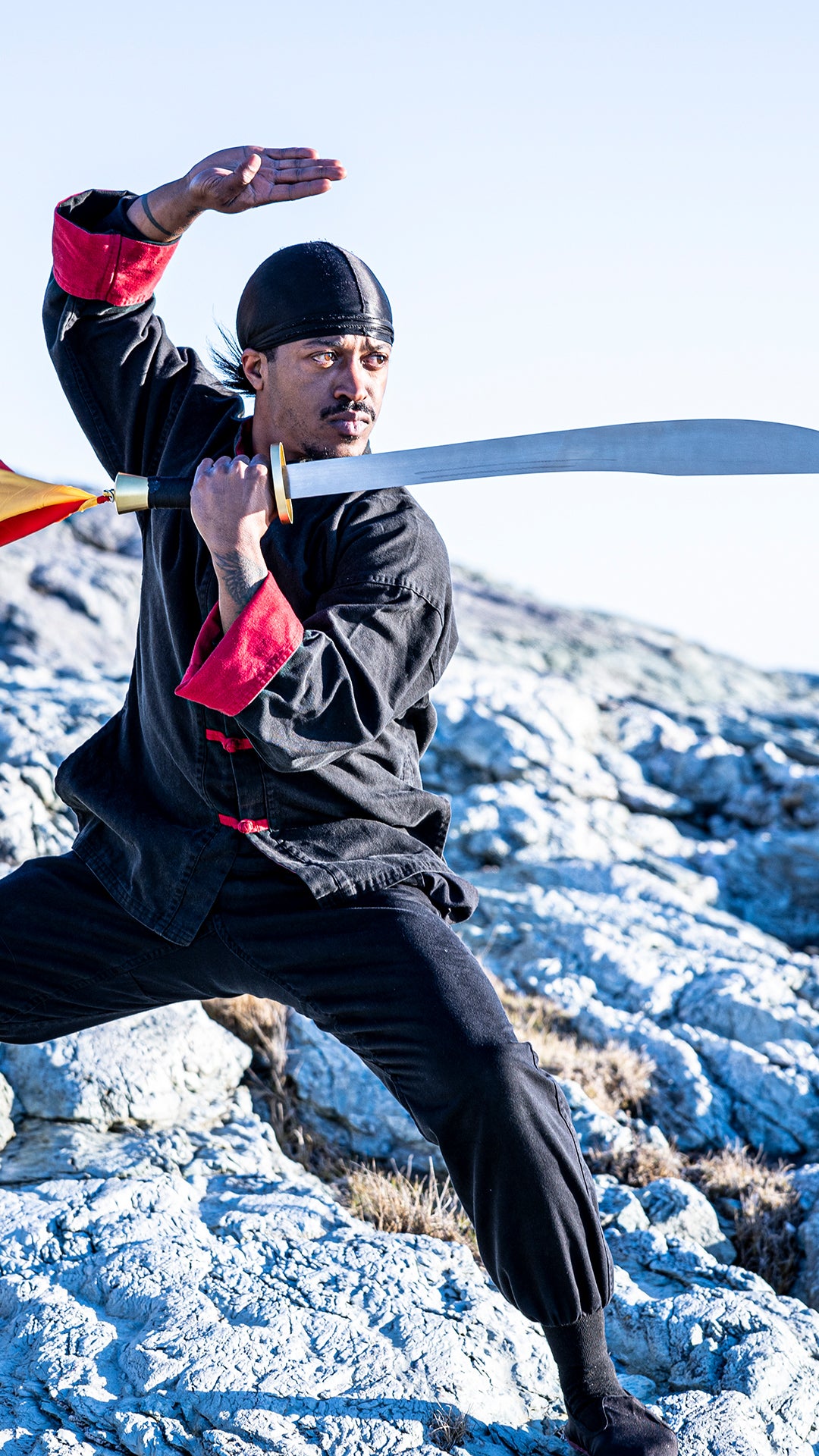 Rob Campbell with sword and in Kung Fu uniform on rocks near beach